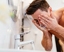 Man washing his face with water from a bathroom tap