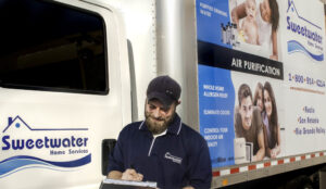 Smiling Sweetwater Home Services technician writing up order in front of a service truck with the company logo on it