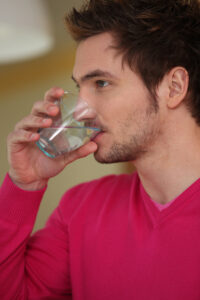 Young man holding a transparent glass of clear water to his mouth to drink