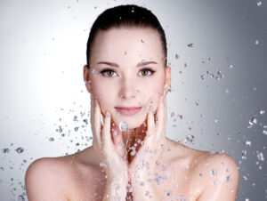 Beautiful bare-shouldered woman with hands at her face and drops of water around her