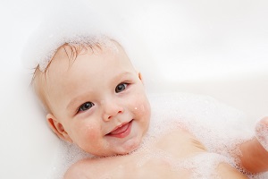 Smiling toothless baby in bathtub suds
