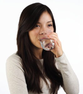 Young woman drinking clear water from a transparent, spotless water glass
