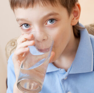 Grade-school-age boy facing camera and drinking from a clear glass of water