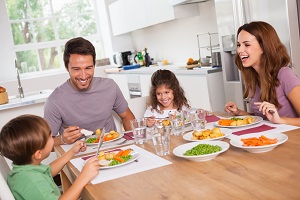 Laughing family of four at kitchen table with full plates and clear glasses of water in front of them