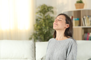 Young woman sitting on living room sofa breathing in the air with her eyes closed